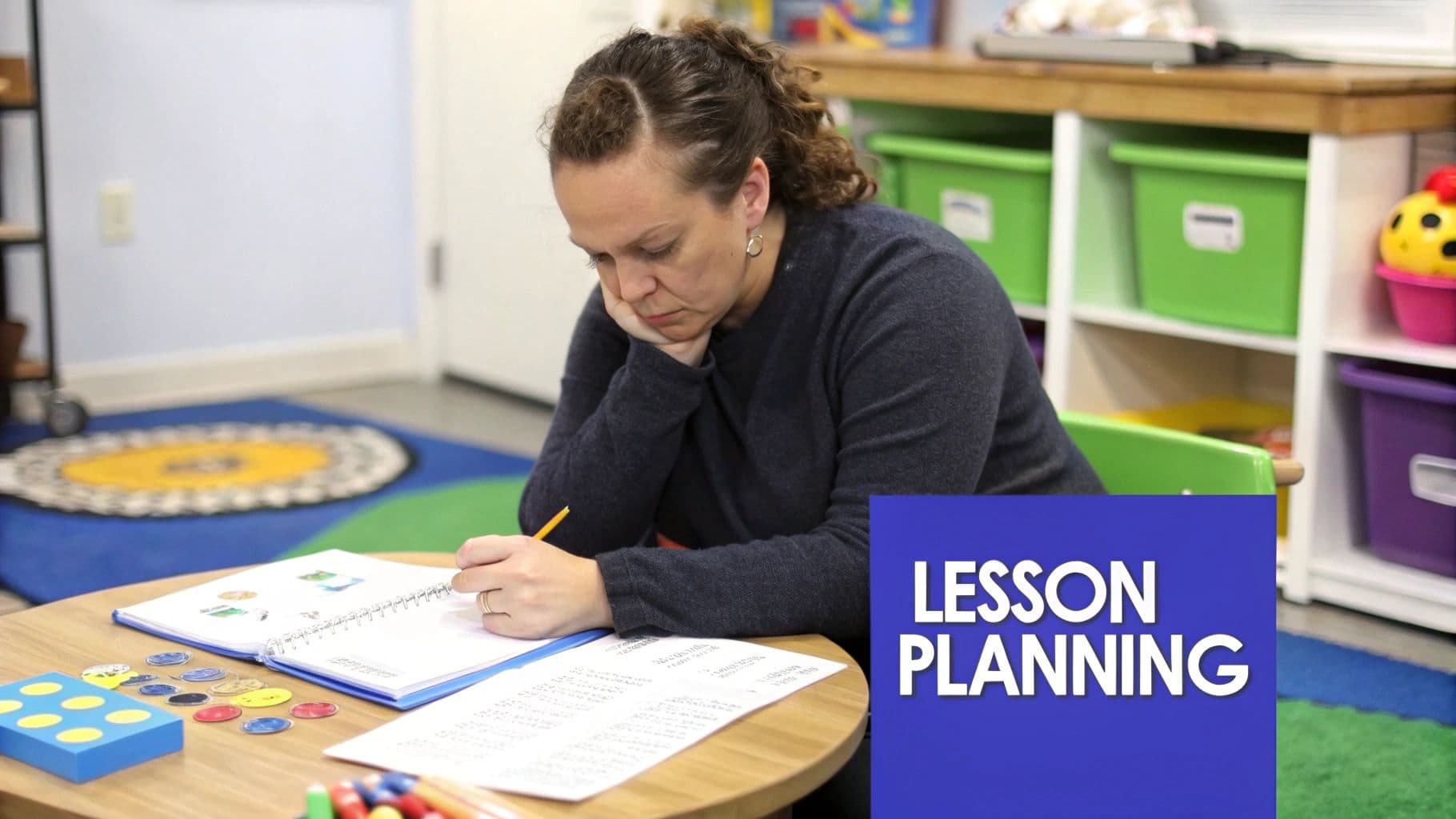 A focused woman sits at a table, writing in a notebook, surrounded by school supplies, lesson planning.