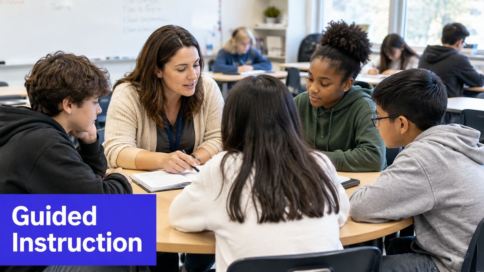 A teacher provides guided instruction to a diverse group of four students around a round classroom table.