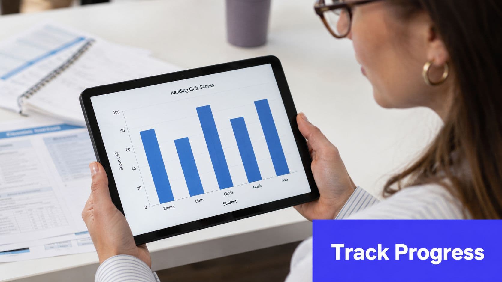 A woman holding a tablet displaying a bar chart showing student reading quiz scores in a classroom.